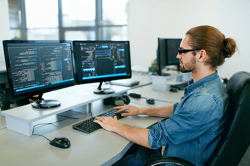 Programación. El hombre que trabaja en la computadora en la oficina de TI, sentado en el escritorio de escritura de códigos. Programador escribiendo código de datos, trabajando en un proyecto en una empresa de desarrollo de software. Imagen de alta calidad.